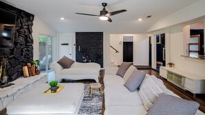 Ein modernes Wohnzimmer mit Steinwand, Kamin, Deckenventilator und Fernseher.