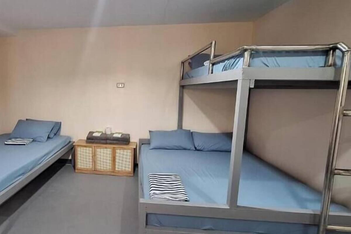 Una habitación con literas, un pequeño armario de madera y una cama individual.