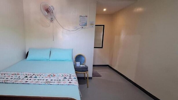 A bedroom with a bed, a chair, a wall-mounted fan, and a poster.