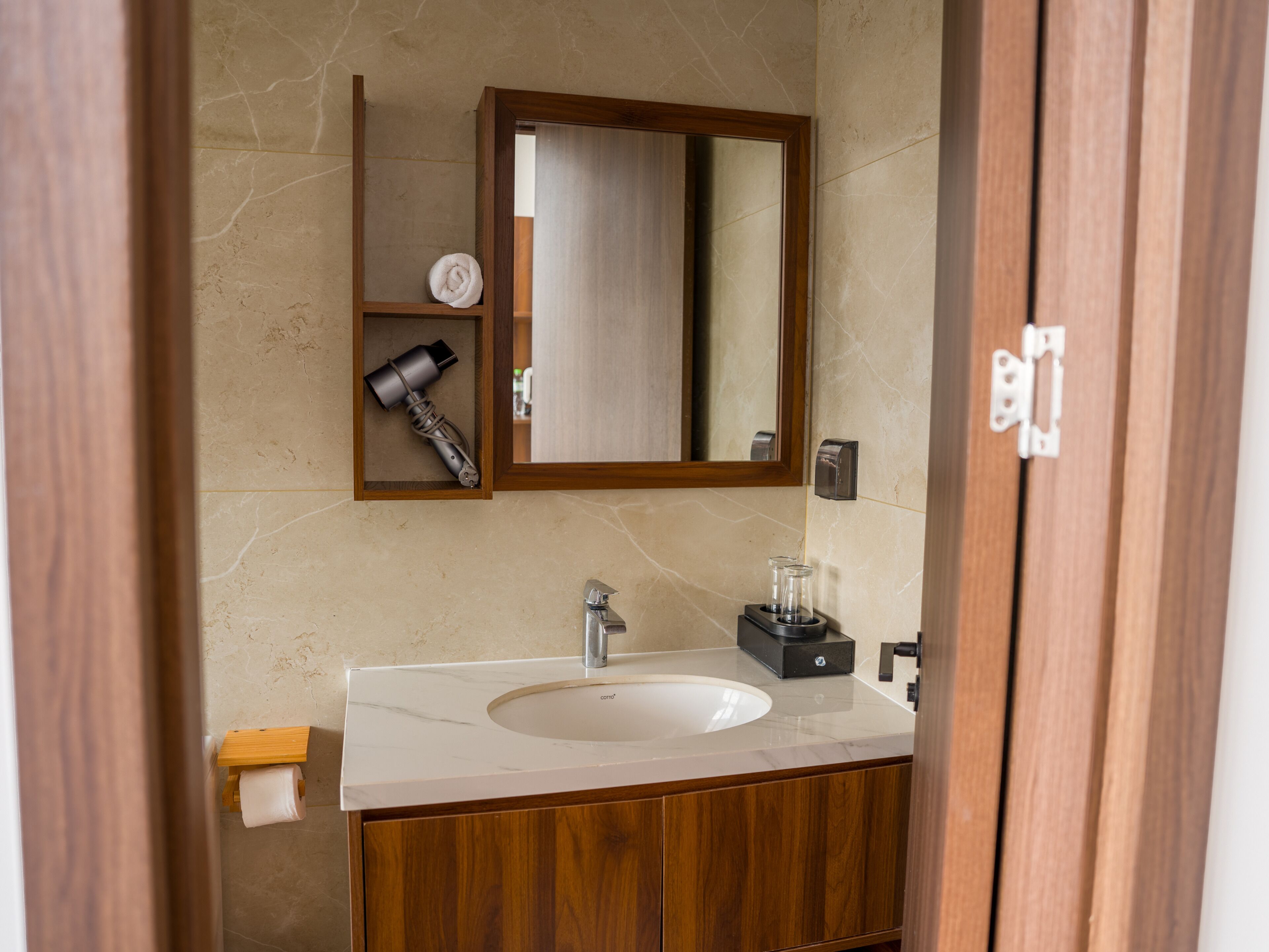 A bathroom with a marble sink, wooden cabinets, a hairdryer, and a mirror.