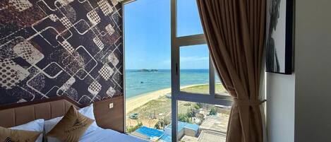 A hotel room with a large window, a bed with white linens, and a patterned wall.