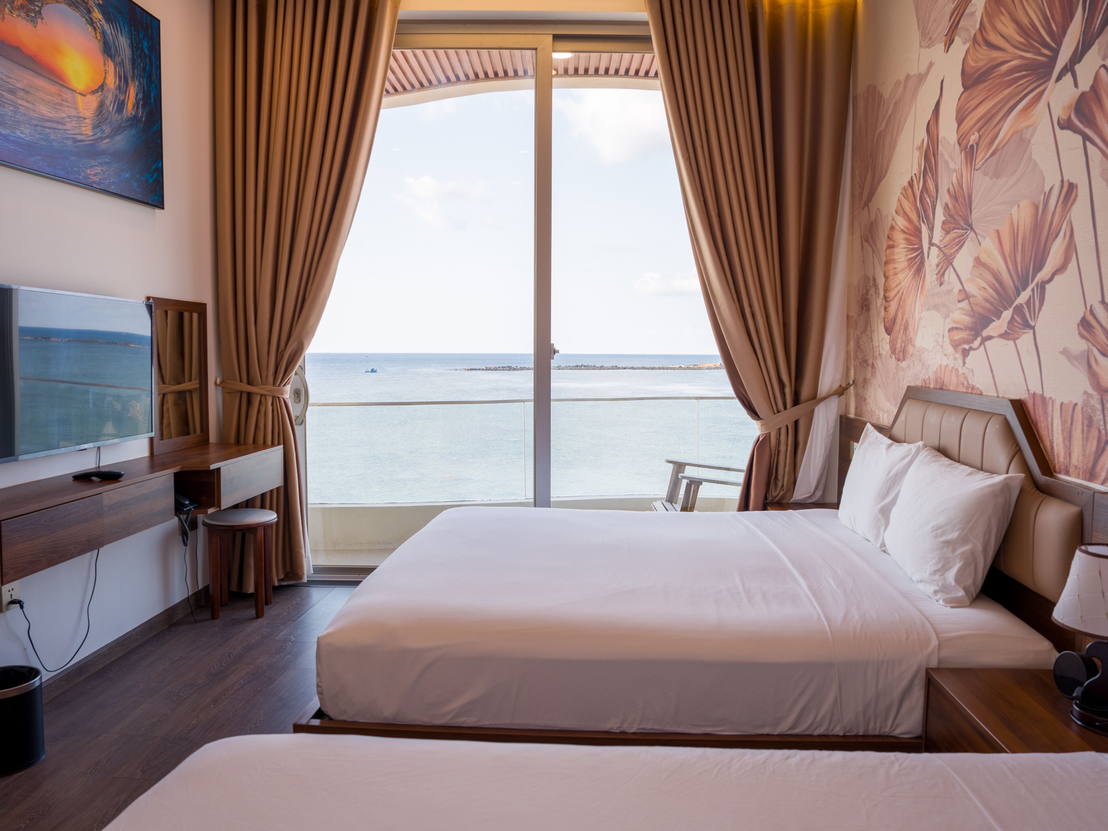 A hotel room with a bed, a TV, a desk, and a view of the sea.