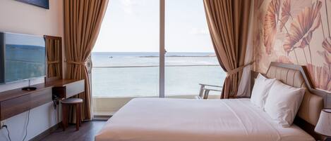 A hotel room with a bed, a TV, a desk, and a view of the sea.