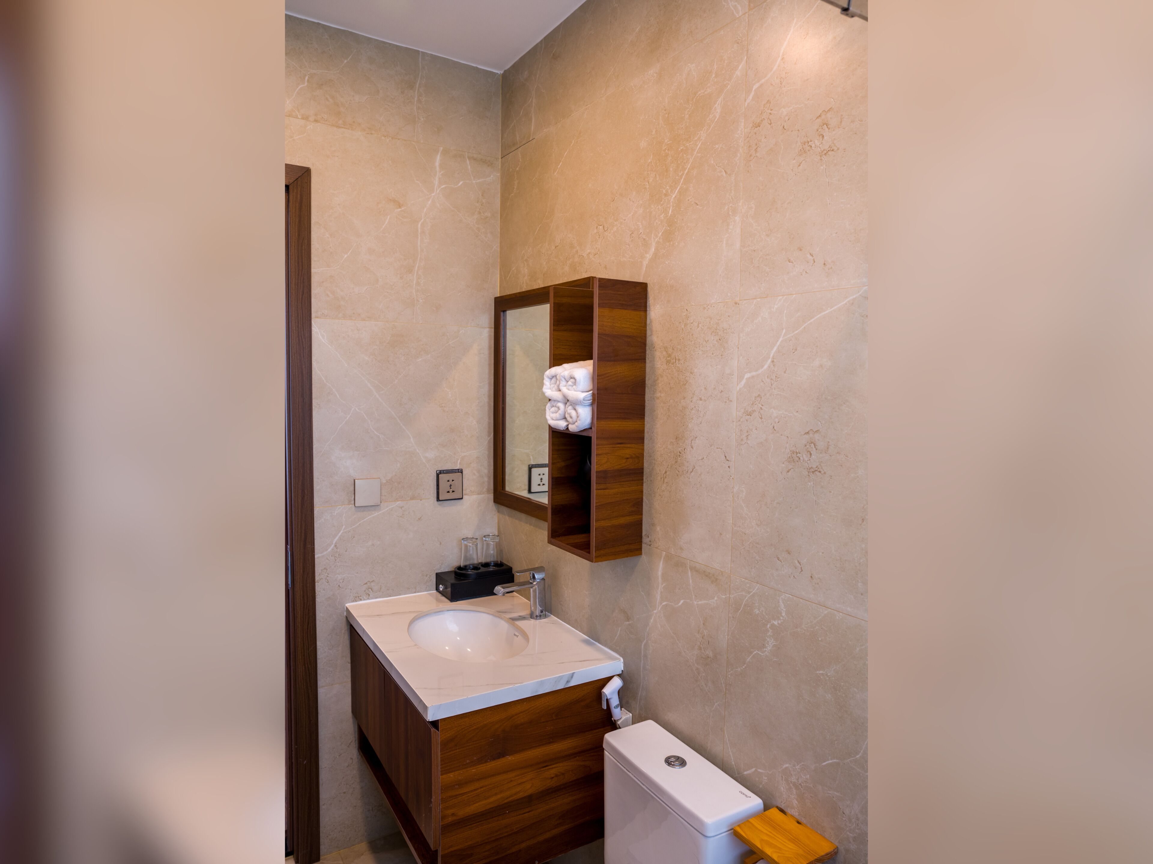 A bathroom with a wooden vanity, a white sink, a mirror, and a toilet.