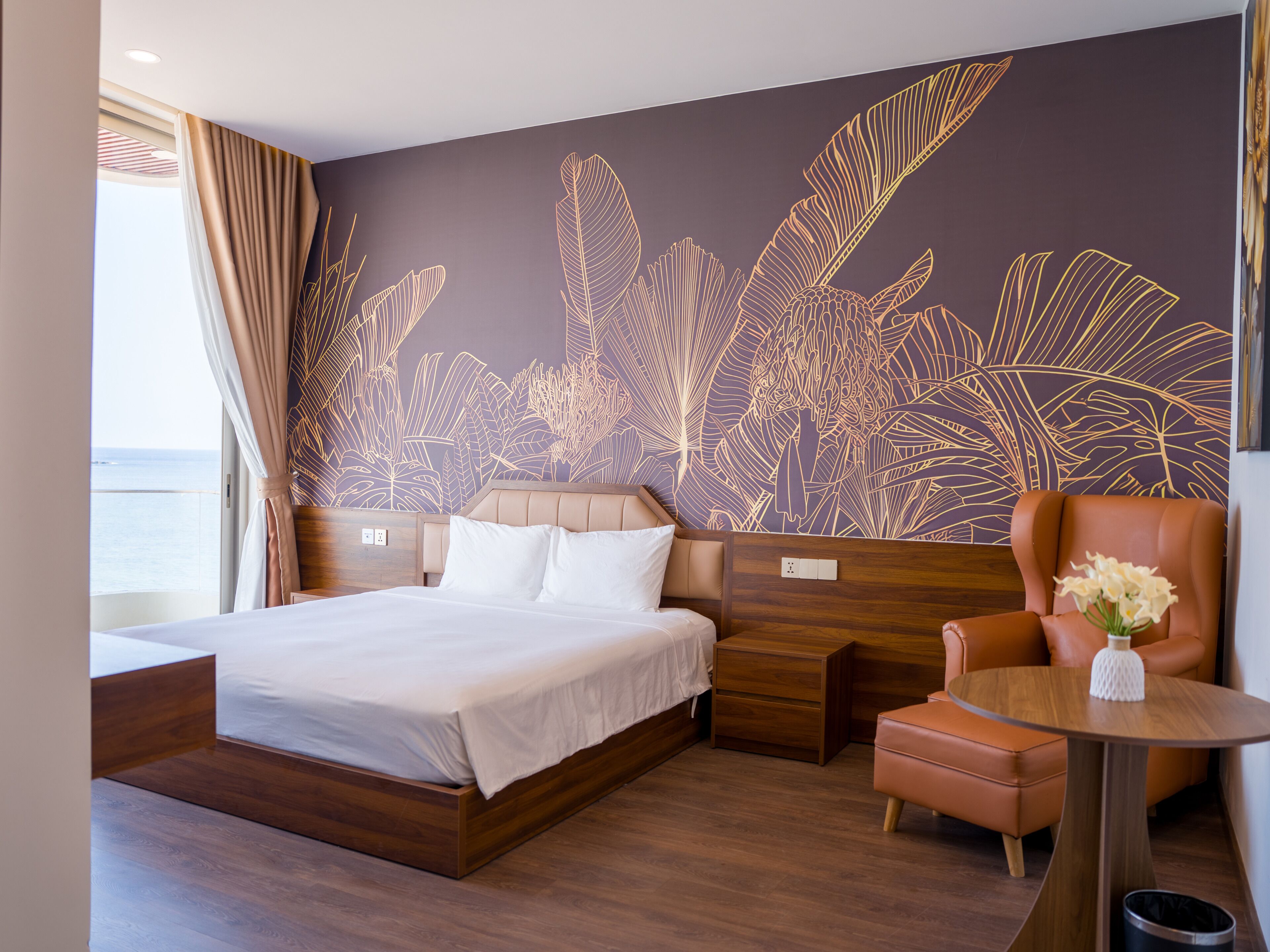 A hotel room with a large bed, a wooden nightstand, a chair, and a small table with a vase.