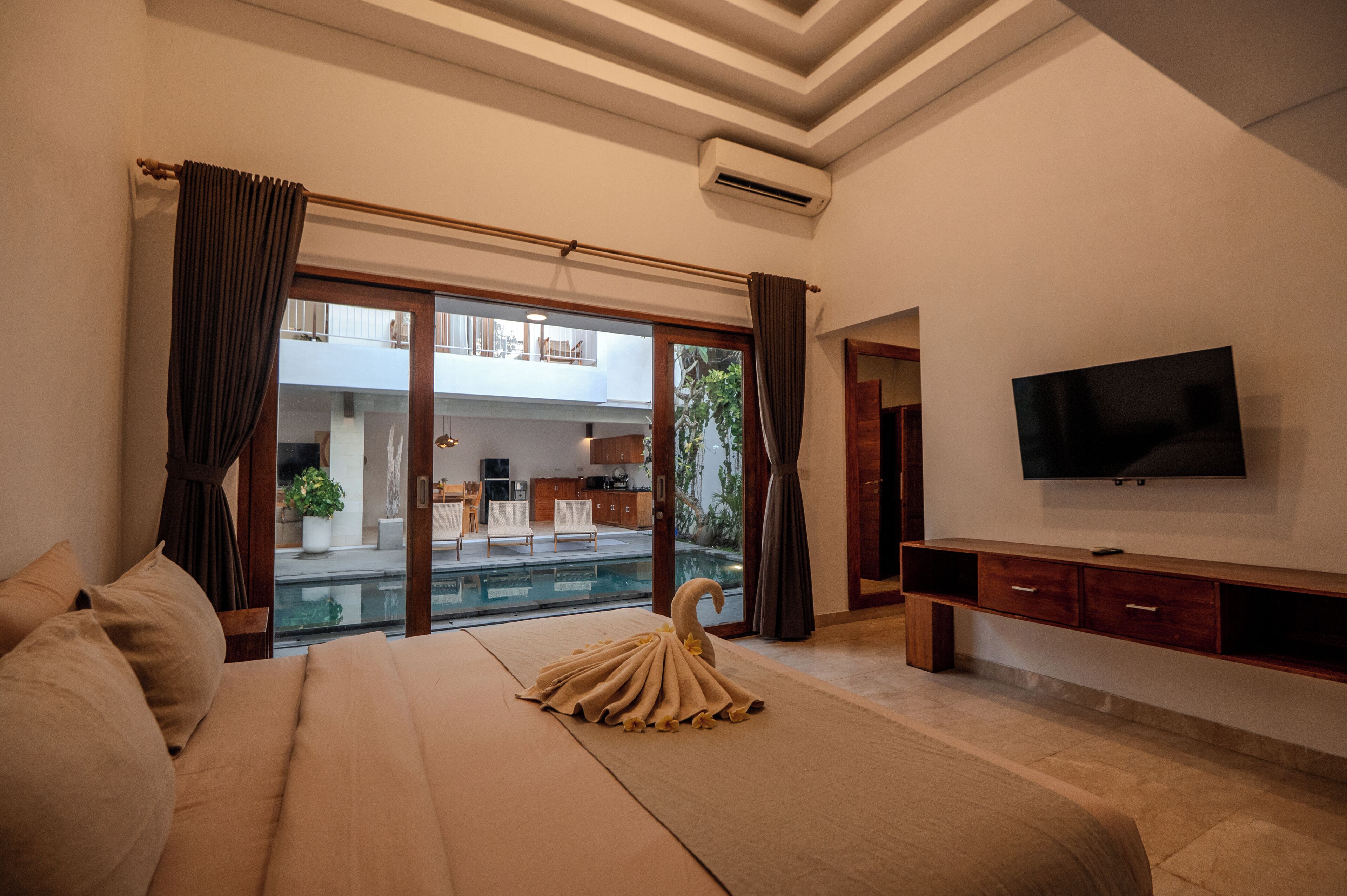 A bedroom with a large bed, a TV, a balcony, and a view of a building.