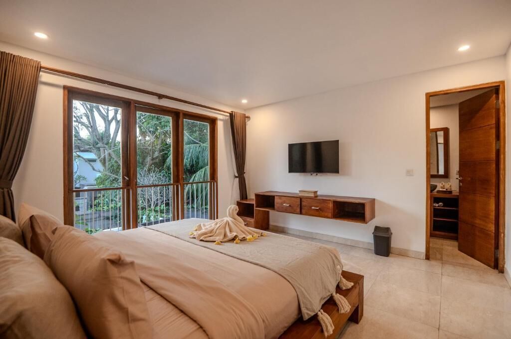 A bedroom with a large bed, a TV mounted on the wall, and a balcony with curtains.