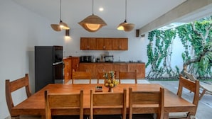 Uma sala de jantar com mesa e cadeiras de madeira, uma fruteira e luminárias pendentes.