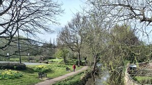 A calm waterway with a stone wall, a paved walkway, and benches.