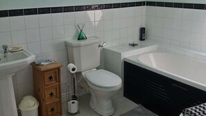 A modern bathroom with a skylight, white tiles, a toilet, a sink, a bathtub, and a small wooden cabinet.
