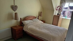 A bedroom with a wooden bed, a nightstand with a lamp, a dresser, and a window with curtains.