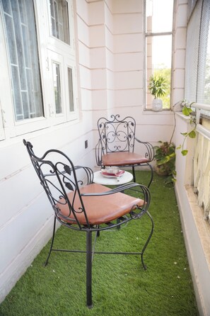 A small outdoor seating area with two metal chairs and a table, surrounded by white walls and a window. - Parkside Haven 3BHK By Avinal (Jaipur)