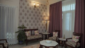 A room with patterned wallpaper, a potted plant, a sofa, two chairs, a small table, and a lamp. - Parkside Haven 3BHK By Avinal (Jaipur)
