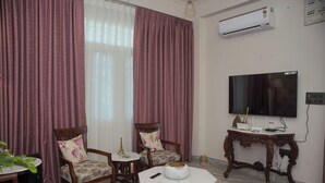 A living room with a TV, two chairs, a table, and an air conditioner. - Parkside Haven 3BHK By Avinal (Jaipur)