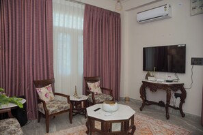 A living room with a TV, two chairs, a table, and an air conditioner. - Parkside Haven 3BHK By Avinal (Jaipur)