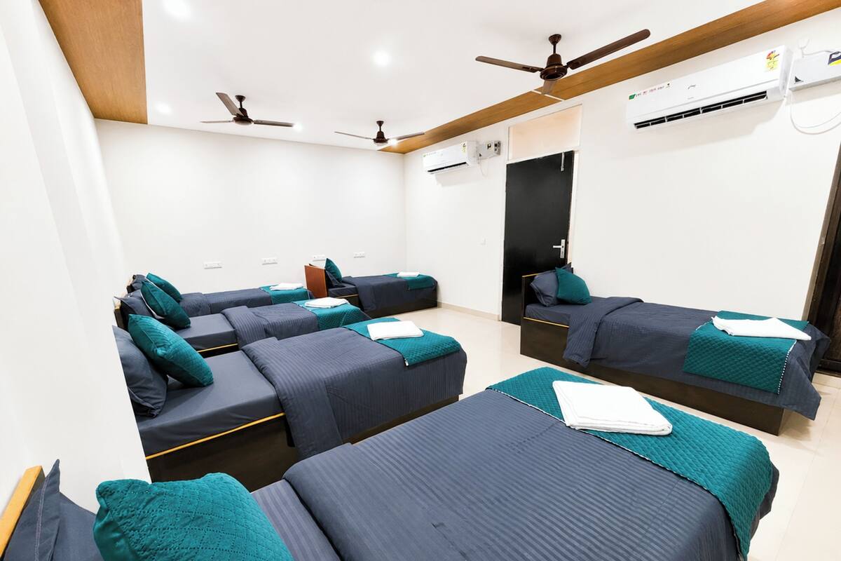 Habitación de hotel con cuatro camas individuales, ventiladores de techo, aire acondicionado y un espejo grande.