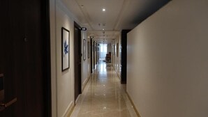 Un largo pasillo de hotel angosto con cuadros en las paredes, puertas numeradas y un suelo de baldosas brillantes.