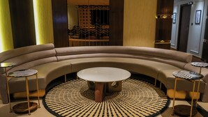 Un sofá curvo con una mesa redonda central, dos mesitas auxiliares y una alfombra con diseño.