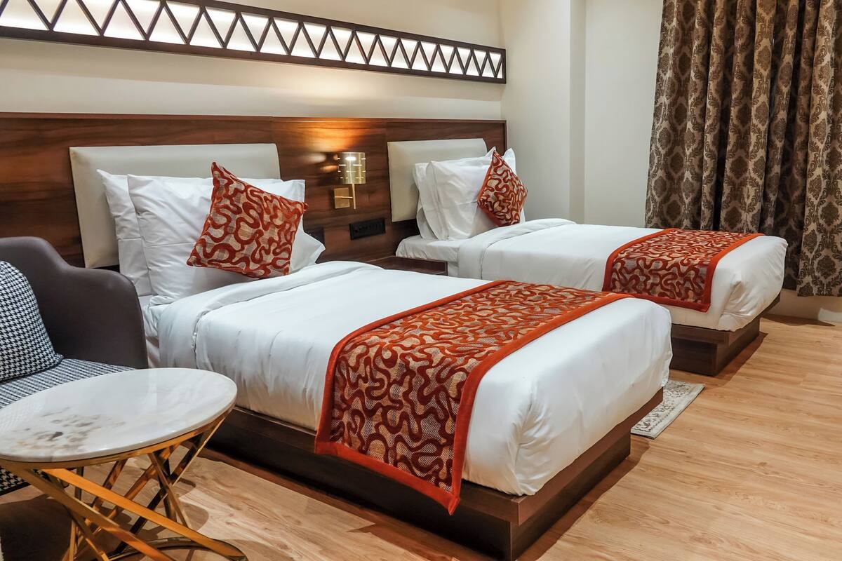 A hotel room with two beds, a small round table, a chair, and a decorative wall panel.
