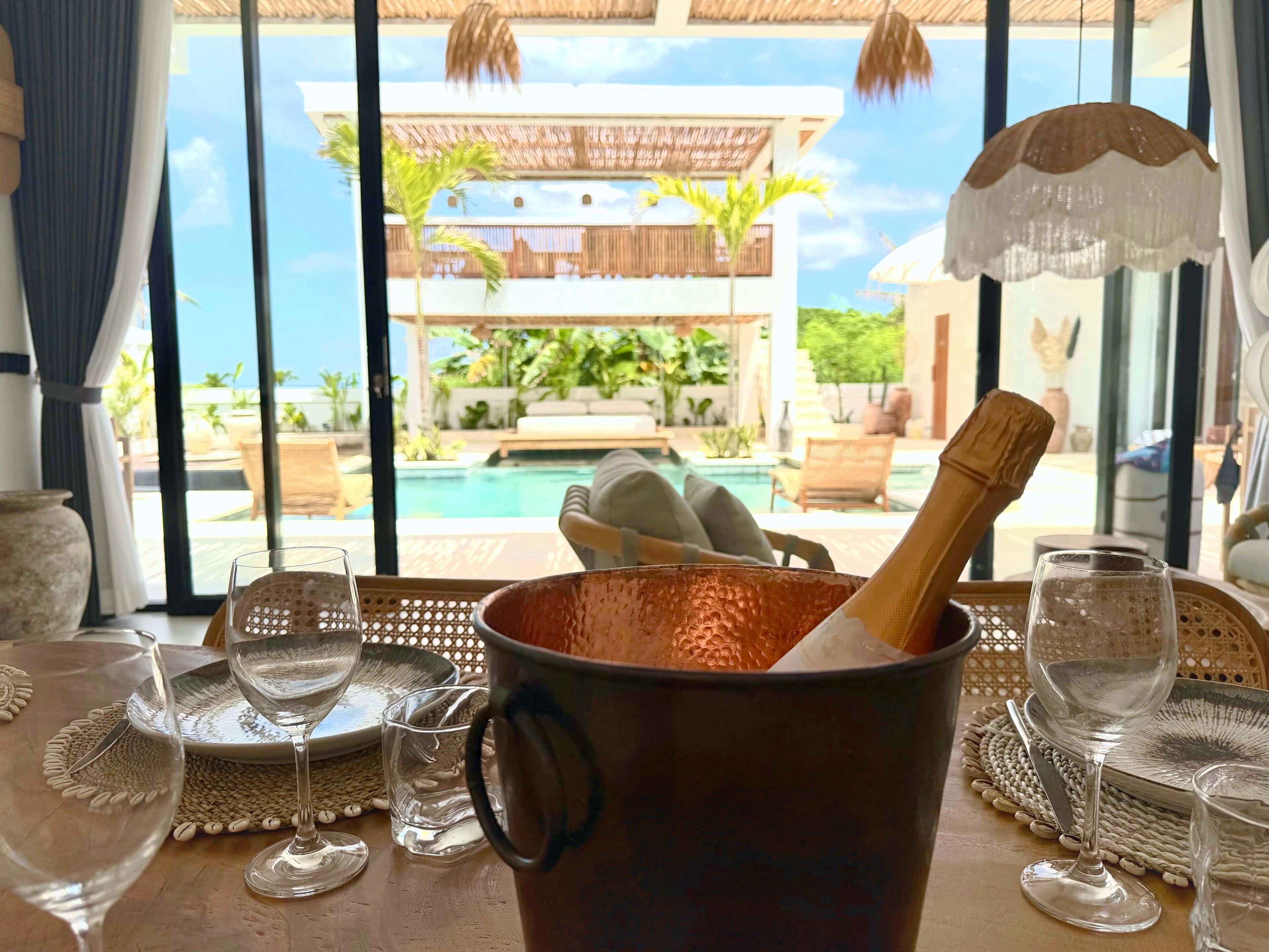 A table with a copper pot, wine glasses, and a view of a pool and outdoor seating area.