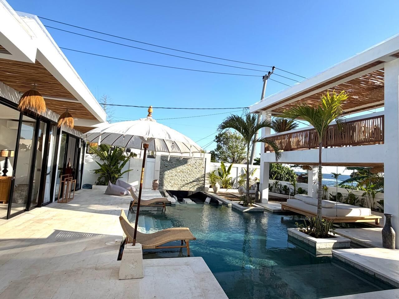 A pool area with lounge chairs, a pergola, and a stone wall.