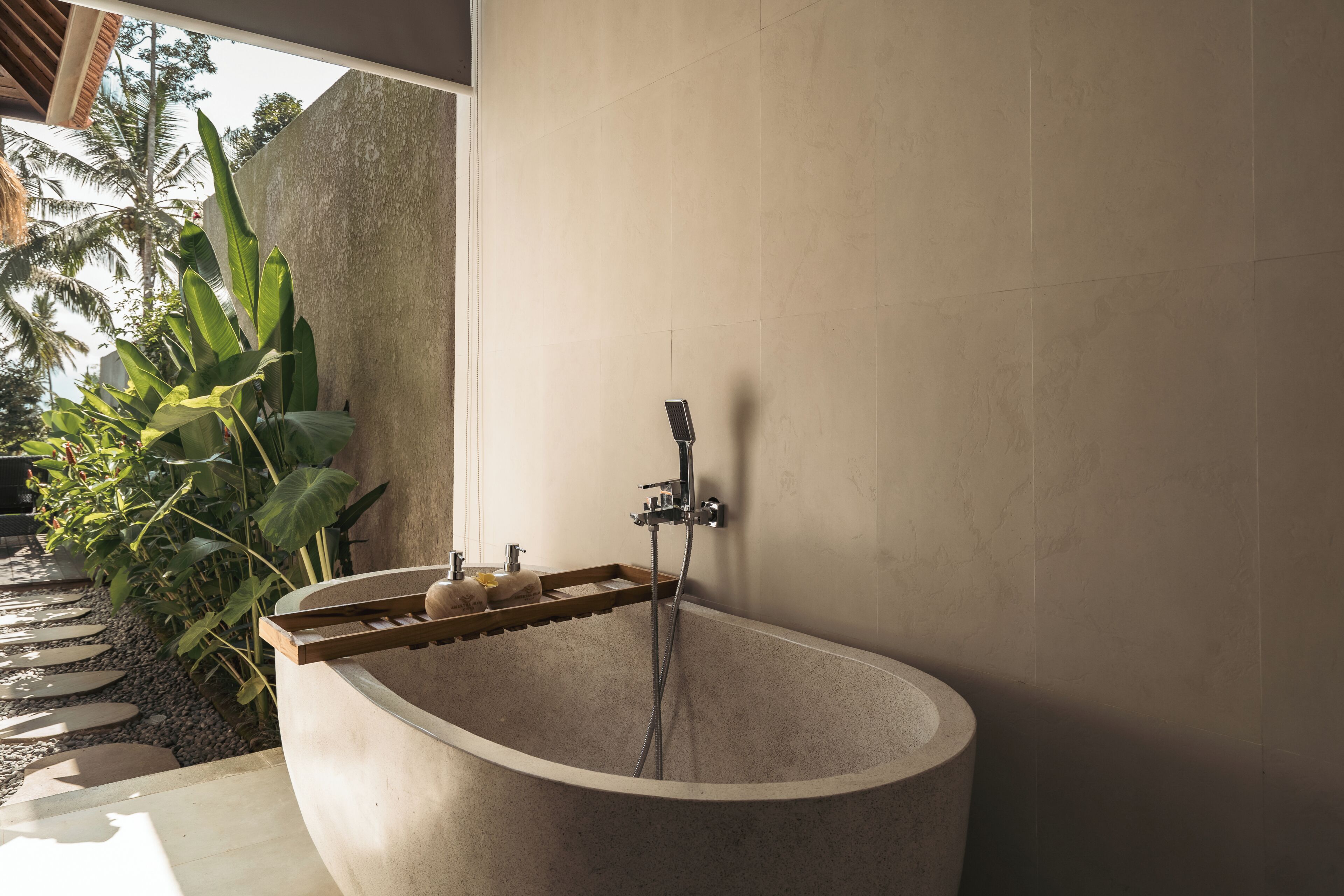 A freestanding bathtub with a showerhead, a wooden shelf, and a stone wall.