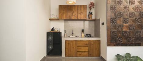 Una cocina con armarios de madera, un refrigerador negro, una lámpara colgante y un panel decorativo en la pared.