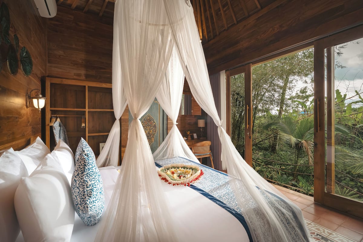 Quarto com cama de dossel, vista para o exterior e decoração em madeira.