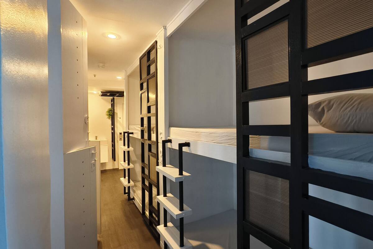 A narrow hallway leading to a bunk bed room with a white door and a small plant.