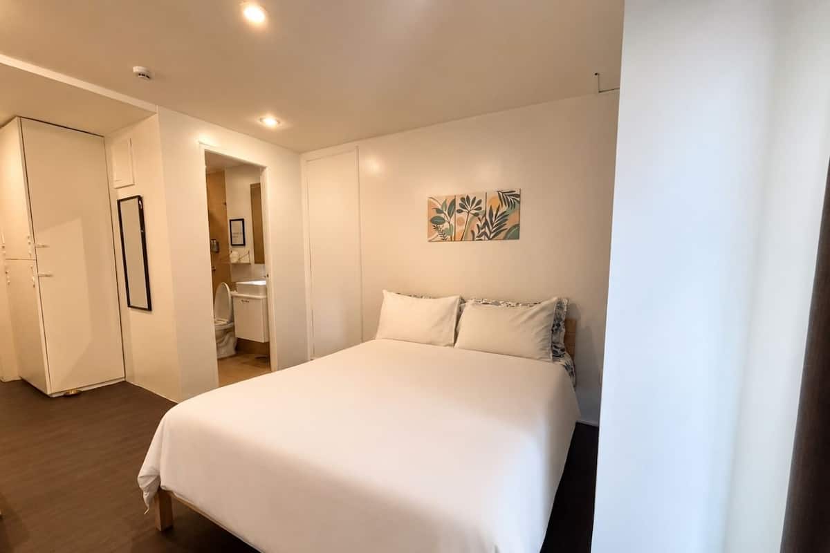A bedroom with a bed, a wardrobe, a bathroom, and a door leading to another room.