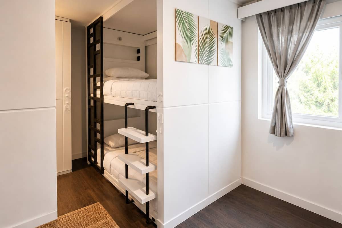 A compact room with a bunk bed, a window with curtains, and wall-mounted artwork.