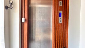 An elevator with a metallic finish, a wall-mounted light fixture, and a fire extinguisher. - V Saigon Suites by SMS Hospitality (Makati)