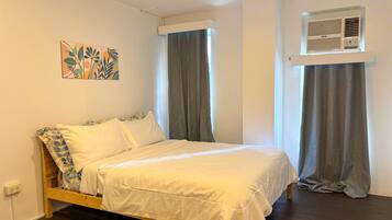 Una cama individual con estructura de madera, ropa de cama blanca y un aire acondicionado de pared.