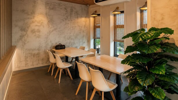 A modern dining area with a wooden table, white chairs, and a large green plant. - V Saigon Suites by SMS Hospitality (Makati)