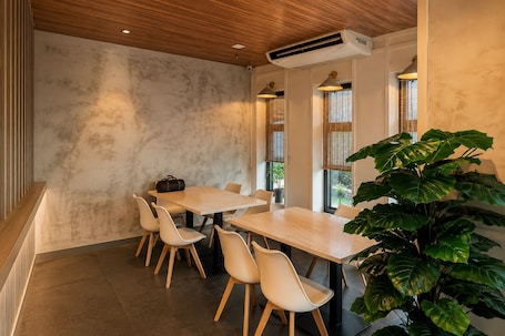 A modern dining area with a wooden table, white chairs, and a large green plant.