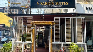 A hotel entrance with a sign for V Saigon Suites Hotel & Restaurant, a bamboo structure, and a nearby shop. - V Saigon Suites by SMS Hospitality (Makati)