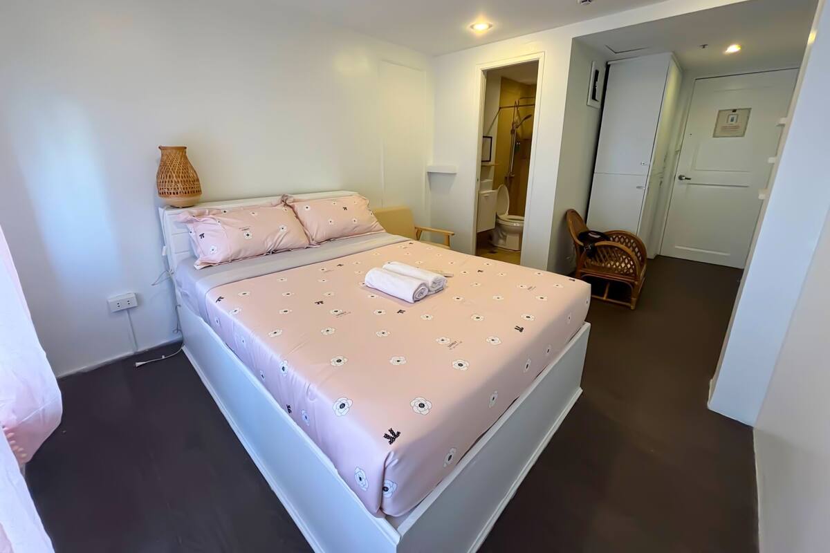 A bedroom with a bed, a bedside table, a chair, a door, and a bathroom visible through an open door.