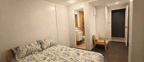 A bedroom with a bed, a chair, and a bathroom visible through an open door.
