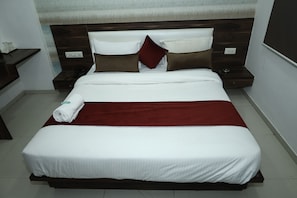 A neatly made bed with white bedding and a red accent, a bedside table with a phone and a remote, and a wall-mounted outlet. - Welcoming 11-bedroom hotel with AC in vibrant Ahmedabad (Ahmedabad)