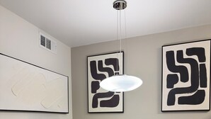 Un coin repas comprenant une table ronde et deux chaises, un luminaire au plafond et deux œuvres d’art abstraites accrochées au mur.