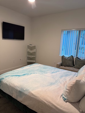 A bedroom with a bed, a TV mounted on the wall, a window with blinds, and a bedside table with a lamp. - Cozy 1-bedroom apartment in Spring Valley, Las Vegas 10 Minutes from Airport (Las Vegas)
