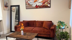 Un salon avec un canapé marron, une table basse, un tableau et une plante en pot.