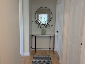 A hallway with a light-colored wall, a white door, a black metal console table, a green vase with branches, and a patterned rug. - FIFA 2026 Modern Luxury Stay-Minutes to SoFi (Inglewood)