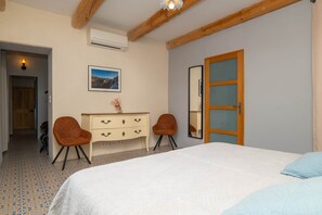Une chambre à coucher comprenant un lit, une commode, deux chaises, un miroir et un appareil de climatisation.