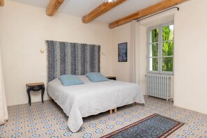 Une chambre à coucher avec un lit, une table de chevet, une fenêtre avec des rideaux et un radiateur.