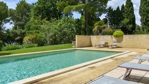 A rectangular swimming pool with clear water, surrounded by a low wall and a small garden area with a few trees and shrubs. - Luberon Cottage at Château Juvenal (Saint-Hippolyte-le-Graveyron)