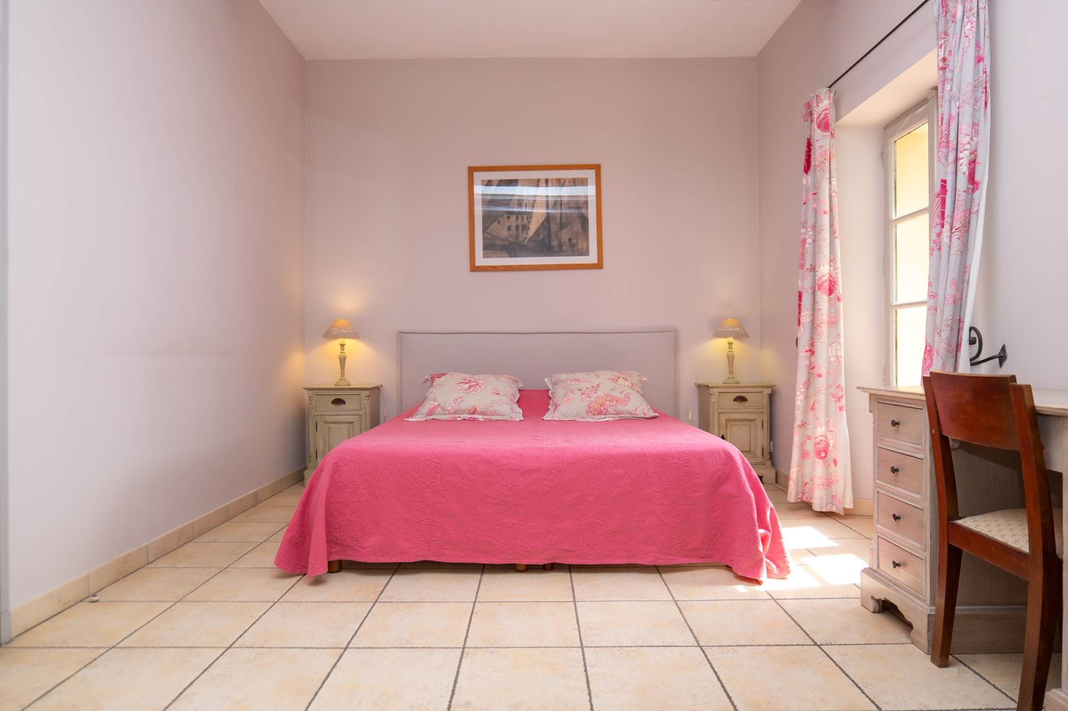 Une chambre à coucher avec un lit, deux tables de chevet avec des lampes, une commode et une fenêtre avec des rideaux.