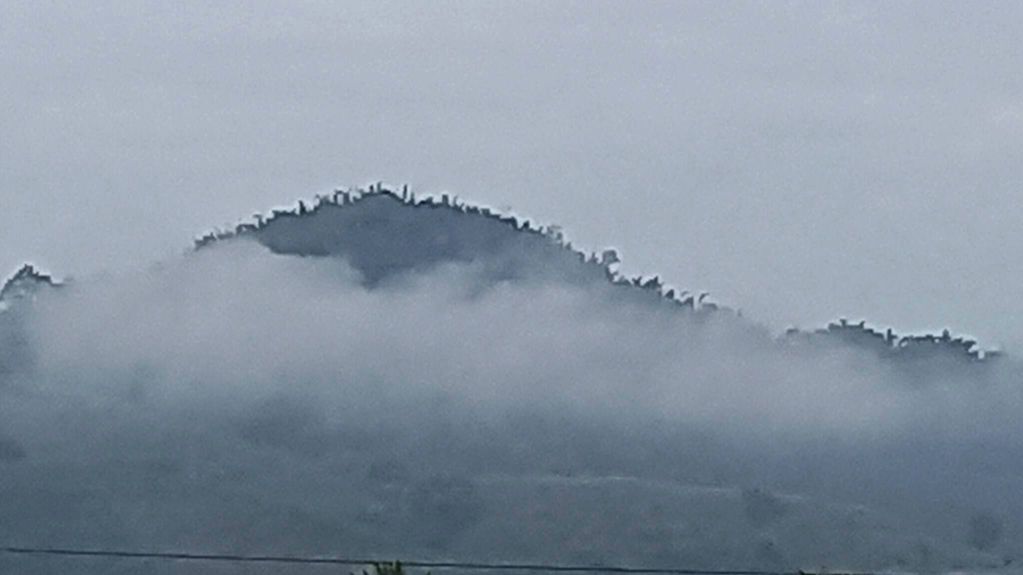 A mountain with a snow-covered peak and a layer of fog or mist at its base.