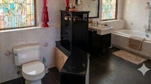 Un bagno con il water, un mobile lavabo nero, un lavandino, una vasca da bagno e una finestra vista bambù.