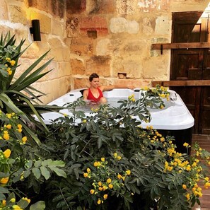 A person in a hot tub with yellow flowers and a stone wall in the background. - Luxury "House of Character" Golden Bay/Manikata. (Mellieha)